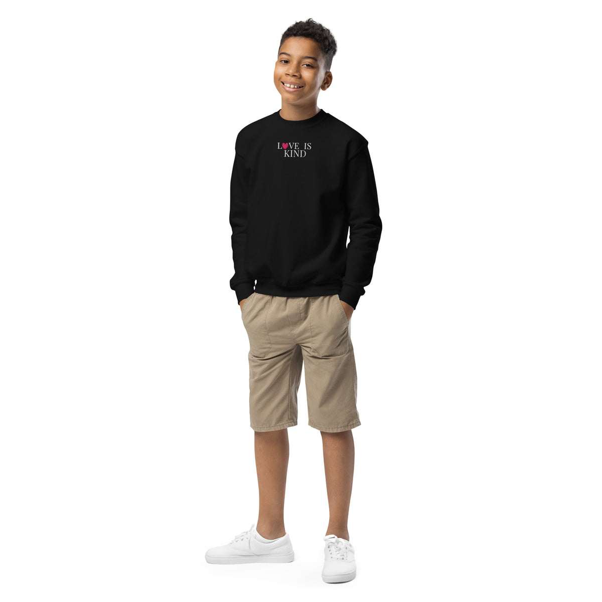 Child wearing a black sweatshirt with 'LOVE IS KIND' text, beige shorts, and white shoes on a white background